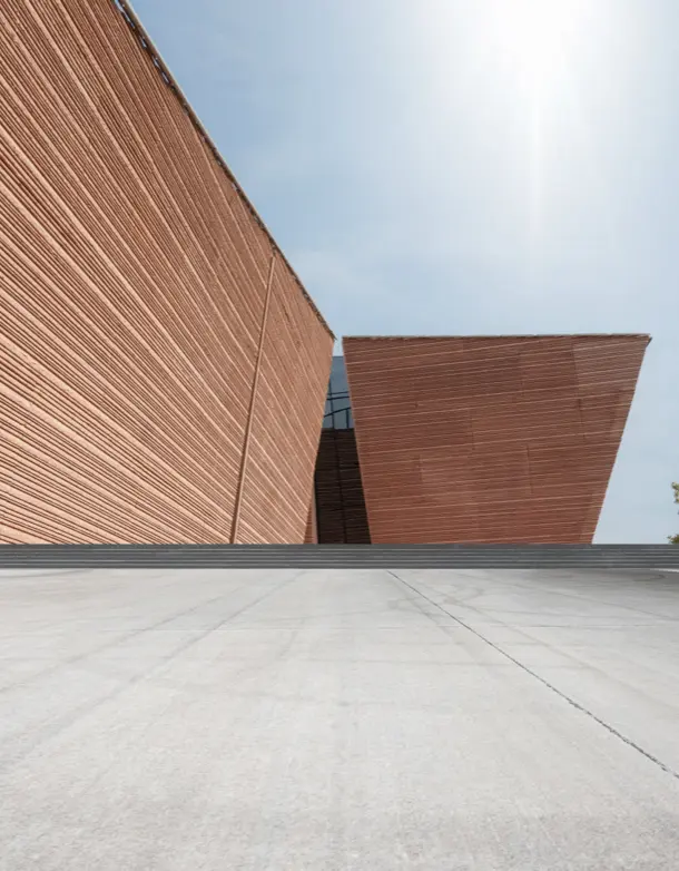 Modern architectural building with angular red walls and large glass windows, set against a clear blue sky, showcasing innovative design elements relevant to VIP Smart Windows and H. Architects.