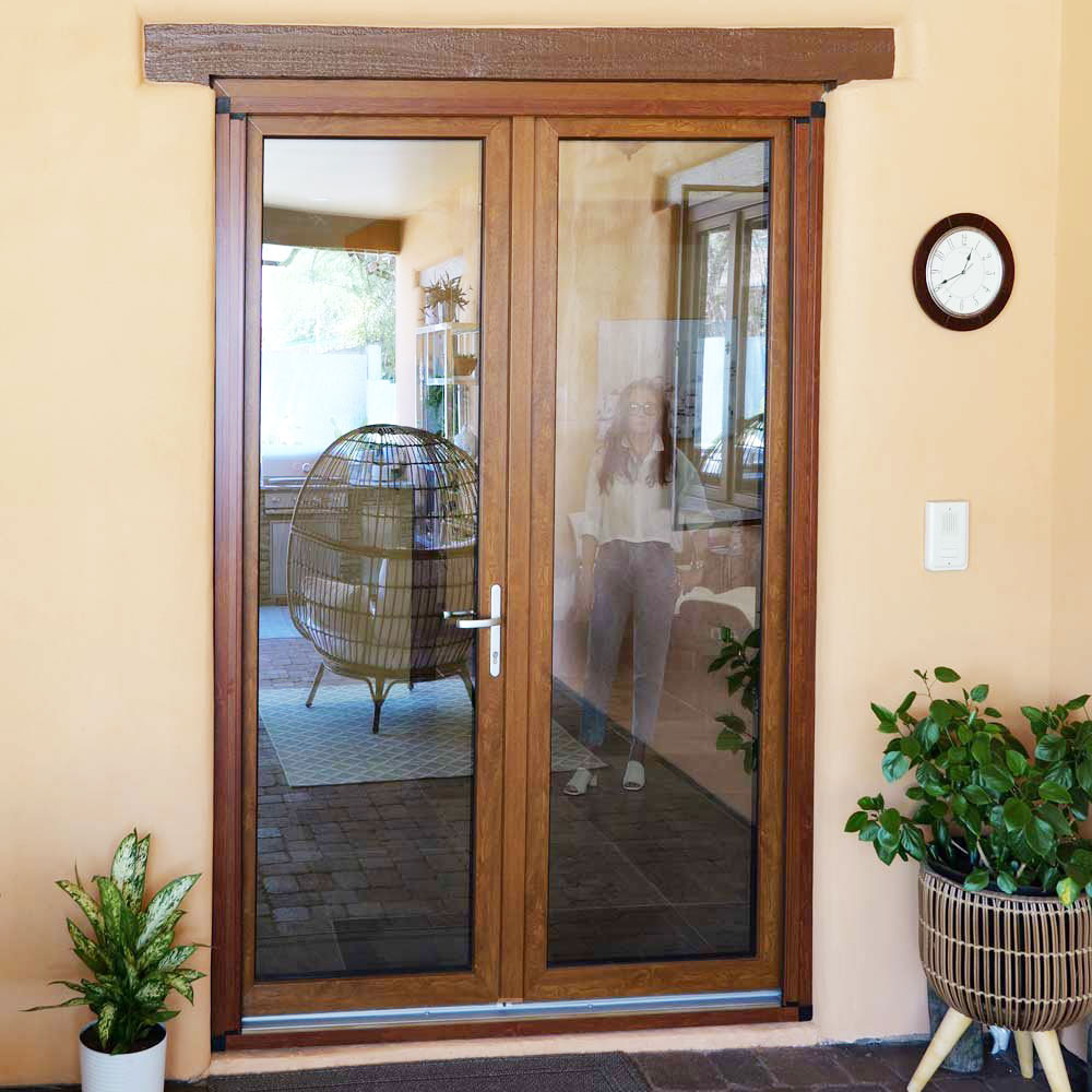 Modern double glass door with wooden frame, showcasing European design, leading to an indoor space with a decorative chair and plants, reflecting VIP Smart Windows' emphasis on quality and aesthetic appeal.
