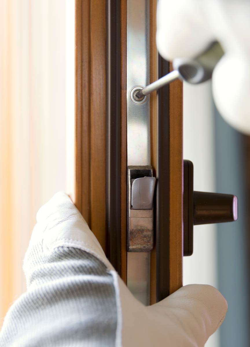 Close-up of a gloved hand using a screwdriver to install a window lock on a wooden frame, emphasizing precision in window installation at VIP Smart Windows.
